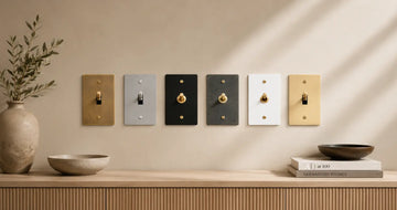 Decorative brass light switch finish samples displayed on a neutral wall, comparing different tones and finishes that may age or tarnish differently over time.