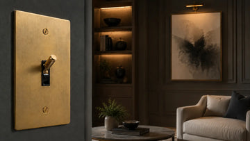 Brass toggle light switch on a dark wall in a luxury living room, showing premium electrical hardware as part of refined interior design.