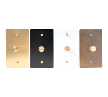 Four rectangular light switch covers in gold, black, white, and bronze on a white background.