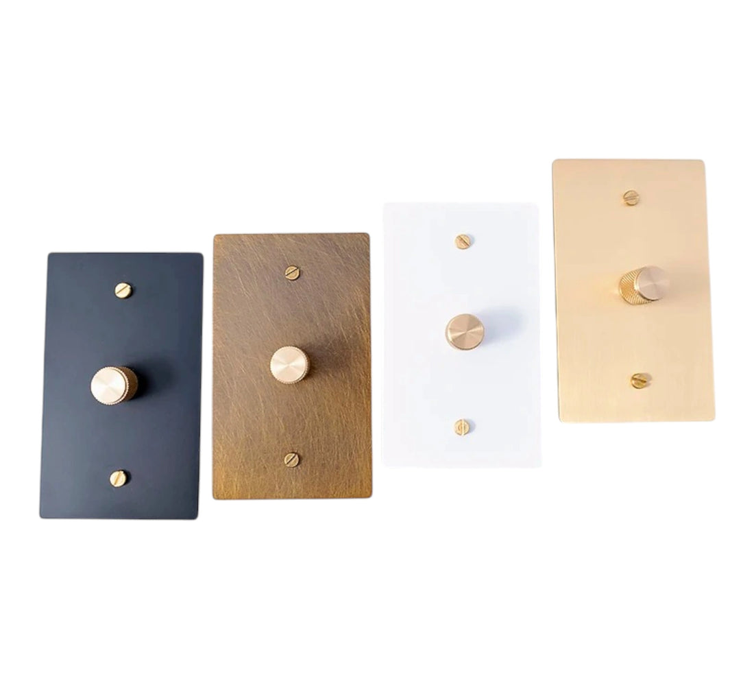 Four rectangular light switch covers in gold, black, white, and bronze on a white background.