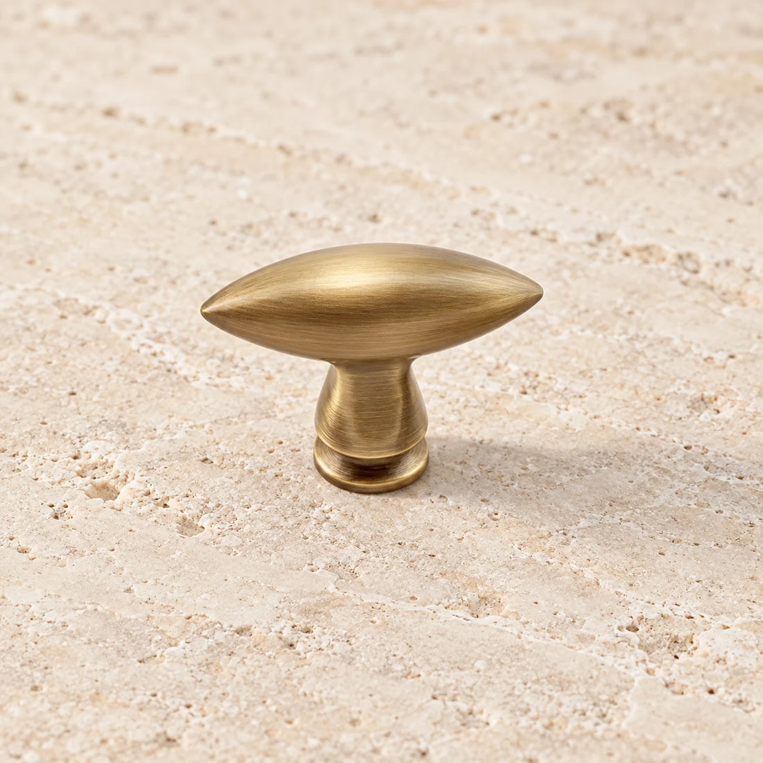 Antique brushed brass olive-shaped cabinet knob on pale limestone