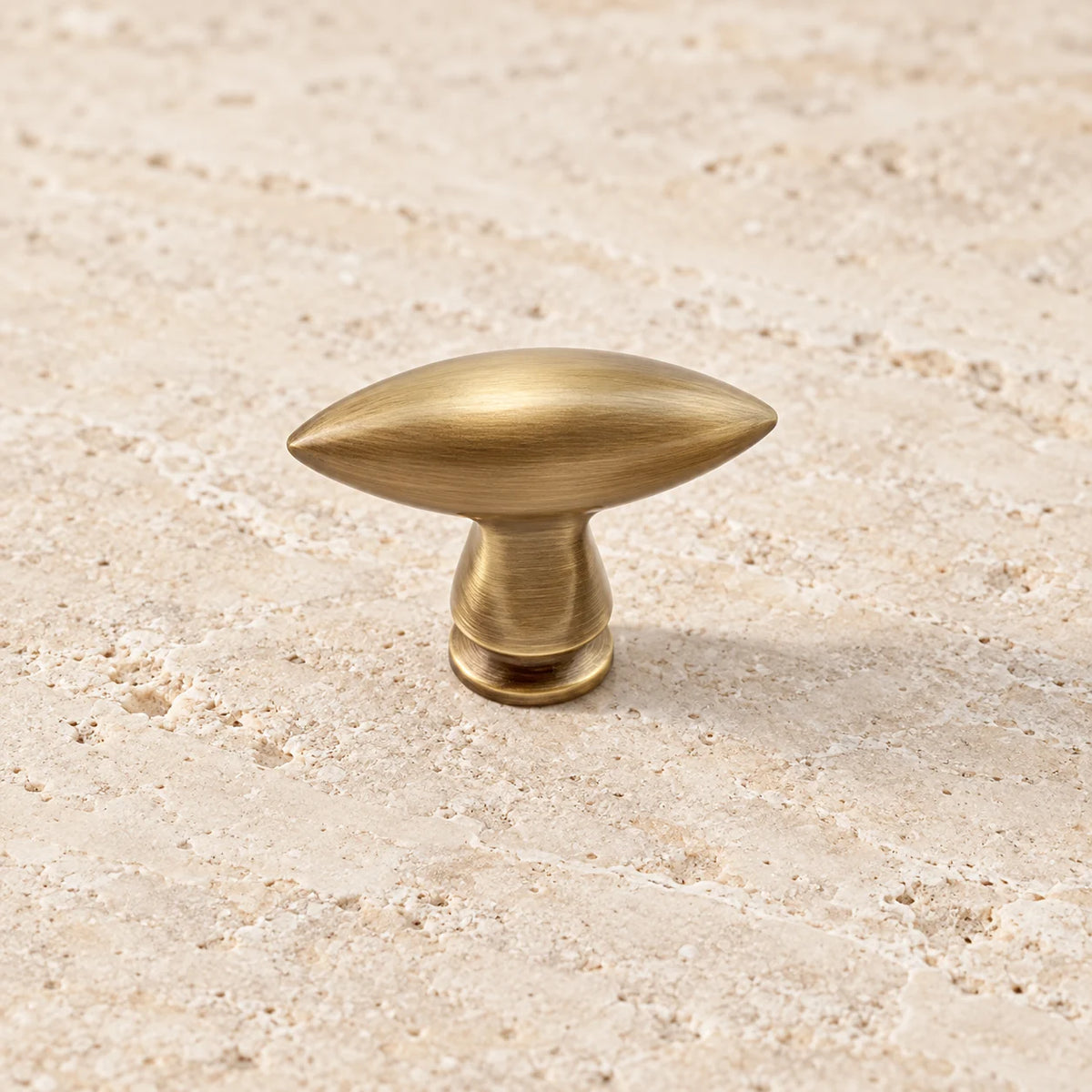 Antique brushed brass olive-shaped cabinet knob on pale limestone