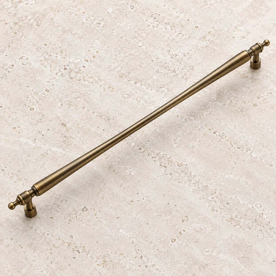 Antique brass long tapered cabinet pull on pale limestone