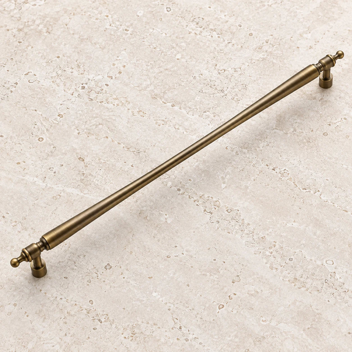 Antique brass long tapered cabinet pull on pale limestone