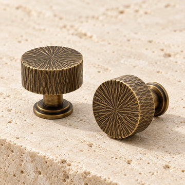 Antique brass radial-textured cabinet knobs arranged on natural limestone
