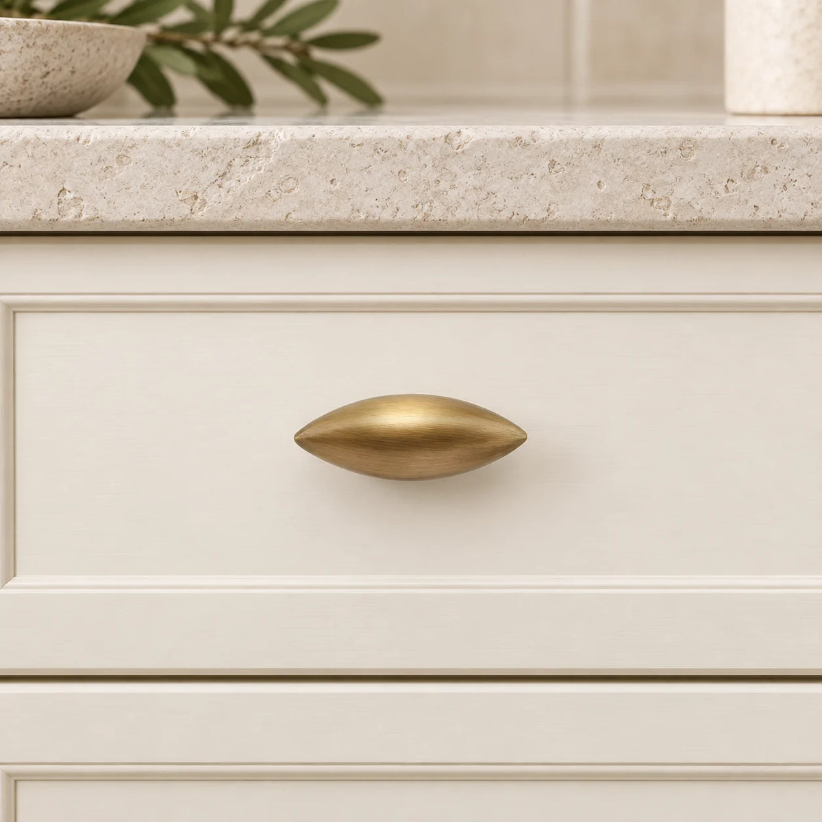 Antique brass olive-shaped knob mounted horizontally on an ivory drawer