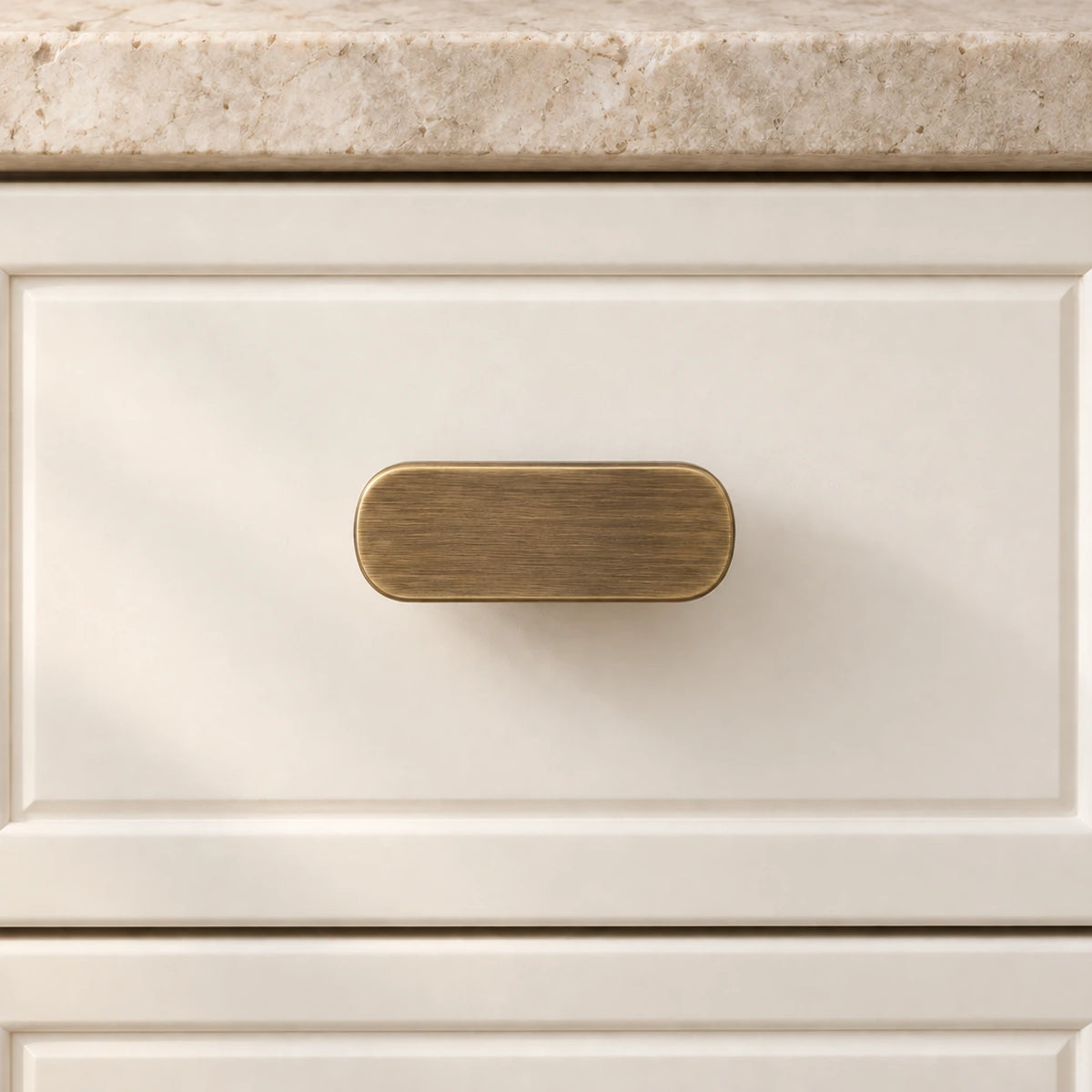 Antique brass rounded T-knob shown from the front on an ivory cabinet drawer