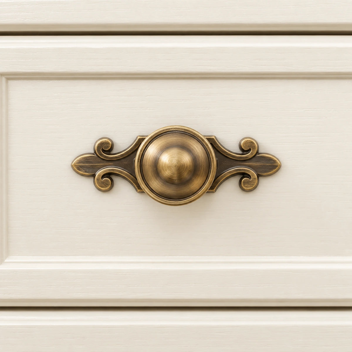 Antique brass domed knob with scroll backplate mounted on an ivory drawer