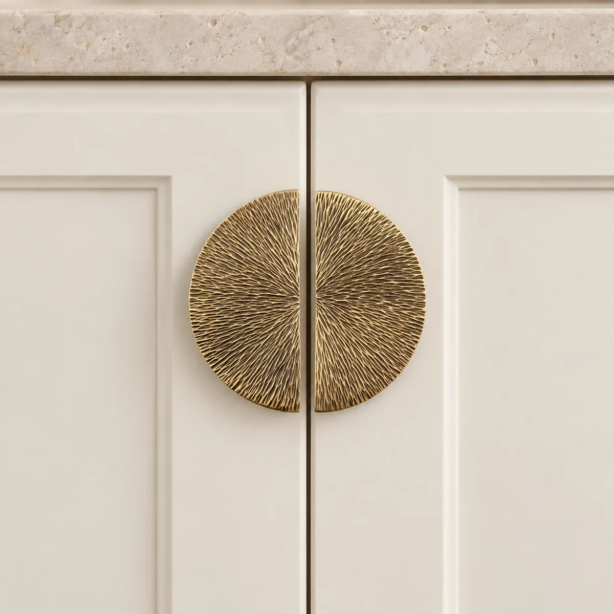 Two antique brass half-moon pulls mounted on adjoining cream cabinet doors