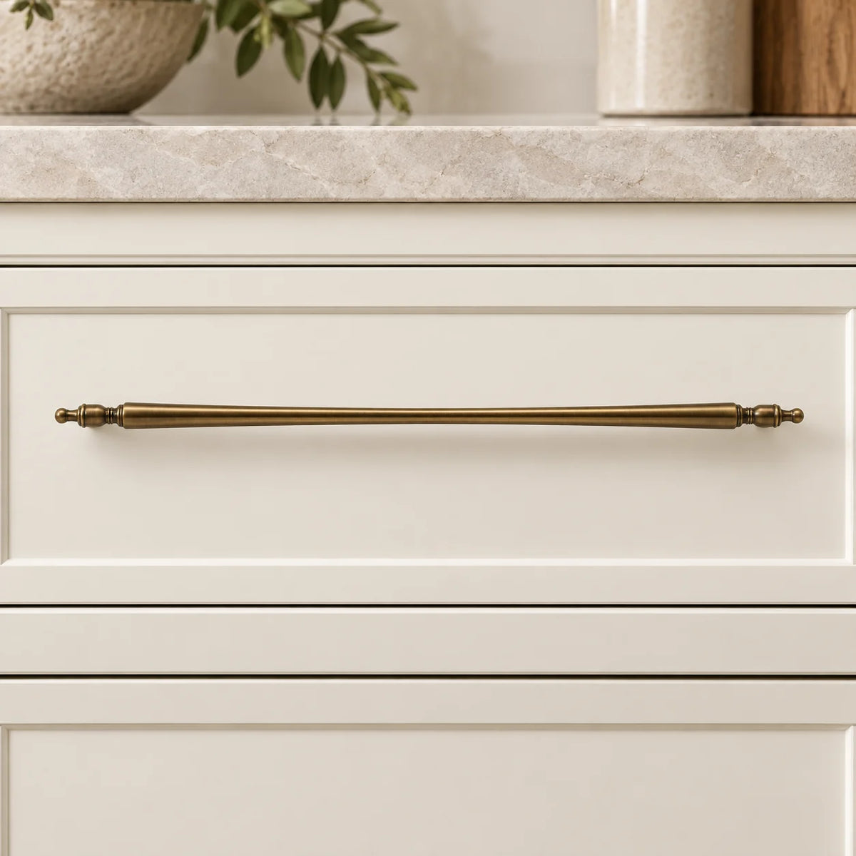 Long antique brass pull mounted horizontally on an ivory drawer
