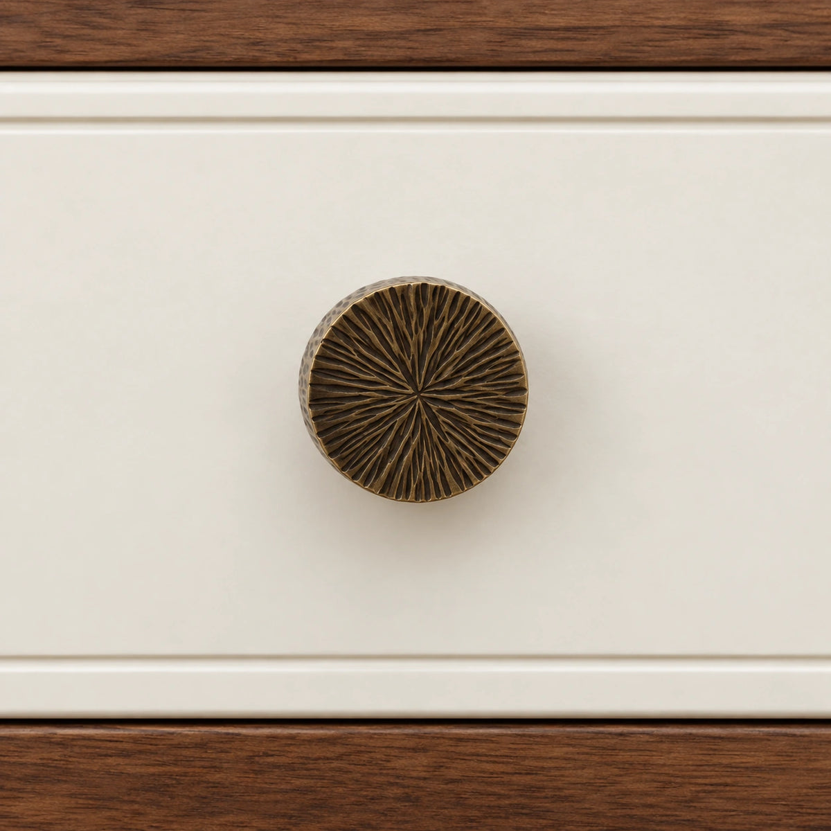 Radial-textured antique brass knob mounted on an ivory drawer front