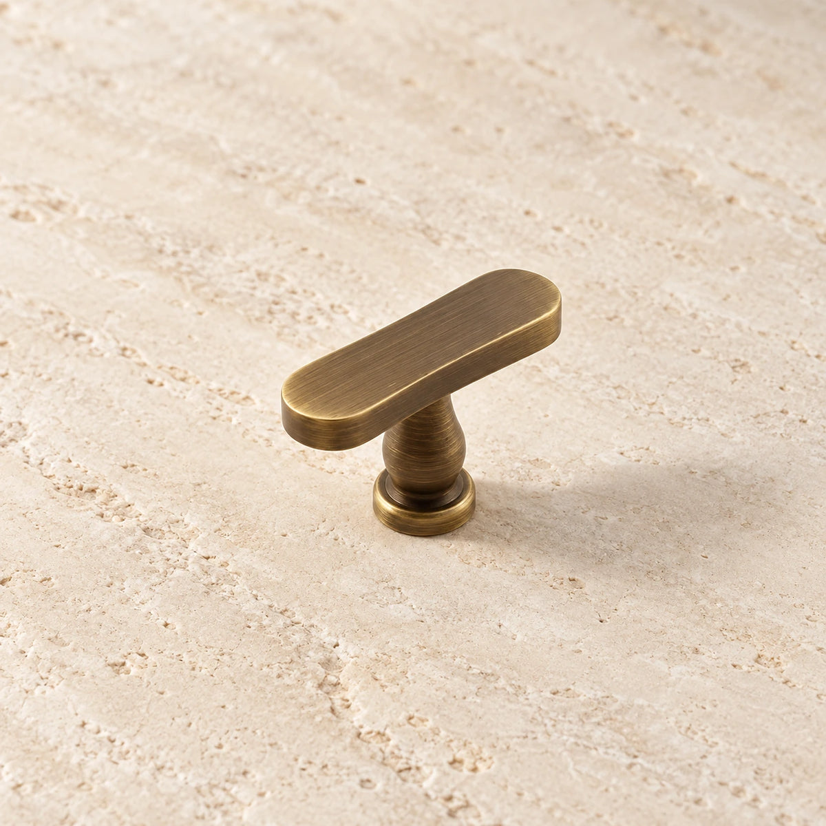 Close view of the rounded rectangular face and turned stem of an antique brass T-knob