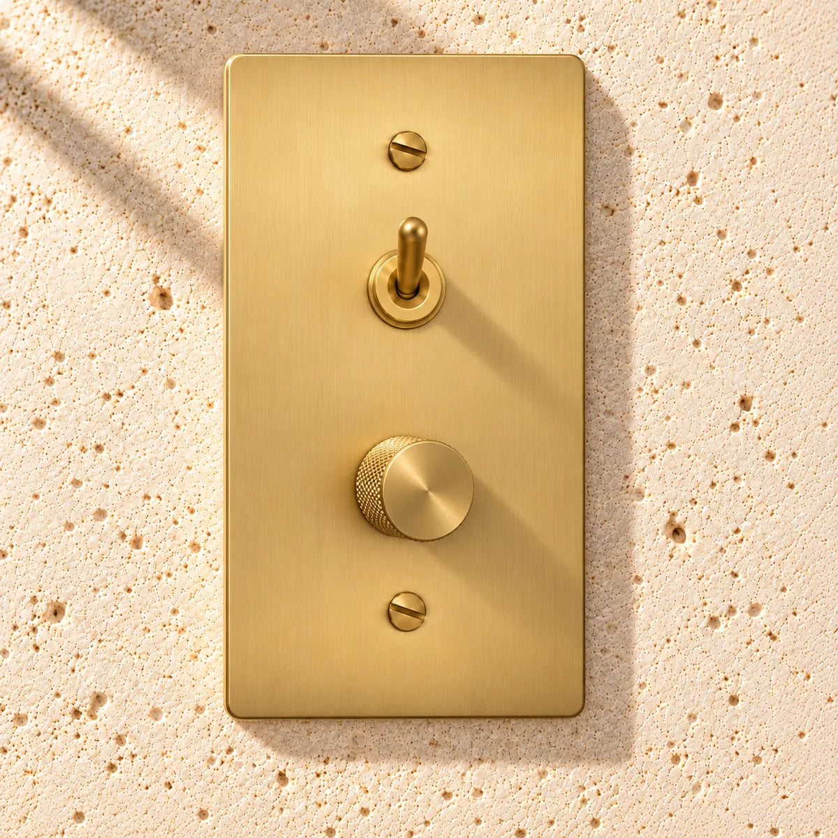 1-gang satin brass smooth toggle and rotary dimmer combination on sunlit limestone, showing the knurled knob depth