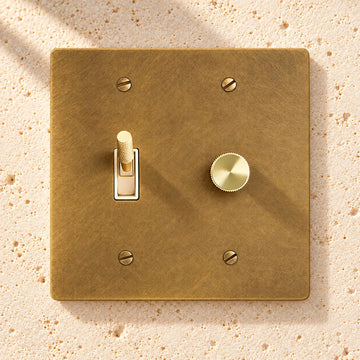 2-Gang Solid Brass Rotary Dimmer + Toggle Switch Combo on sunlit pale limestone
