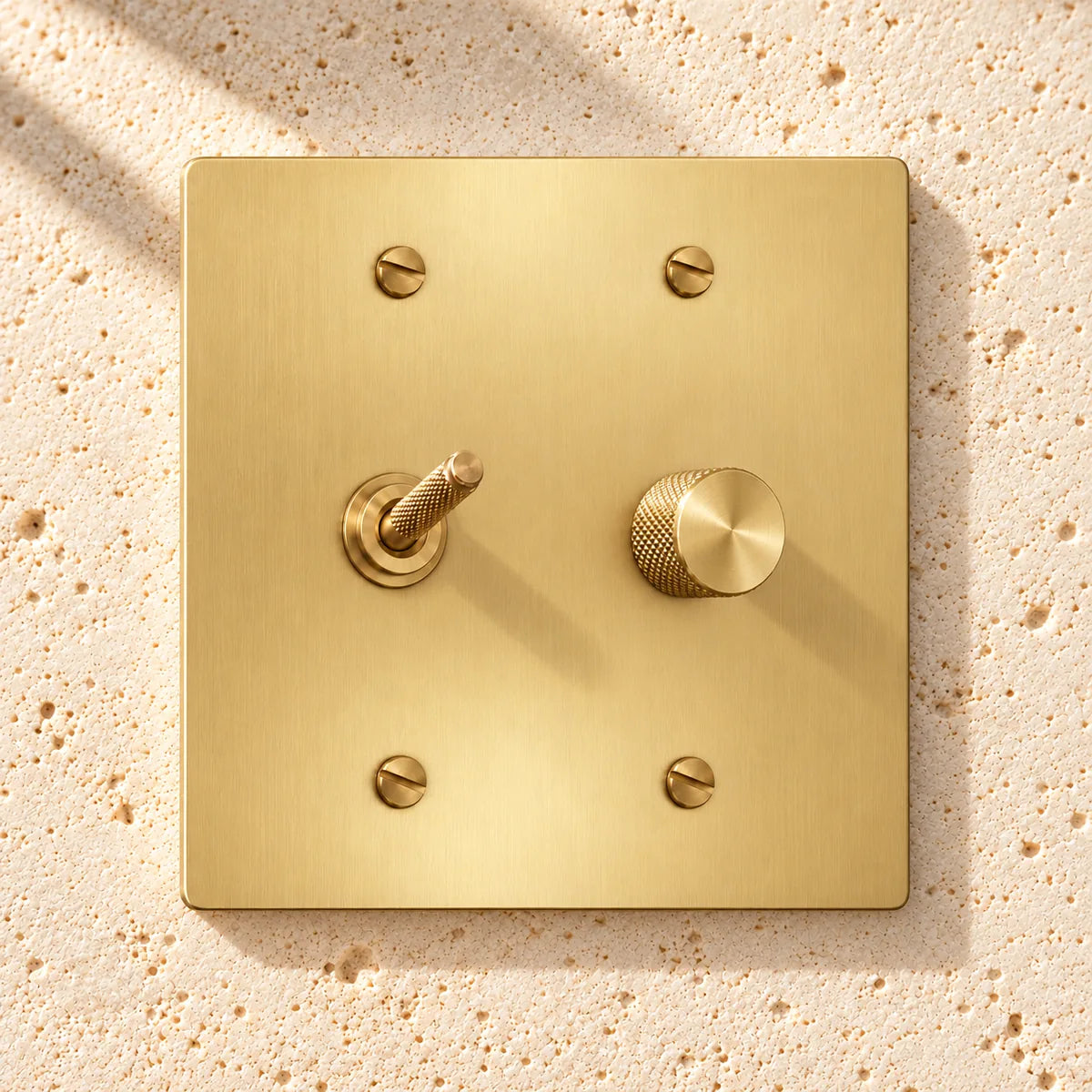 2-Gang Solid Brass Knurled Toggle Light Switch & Rotary Dimmer on sunlit pale limestone