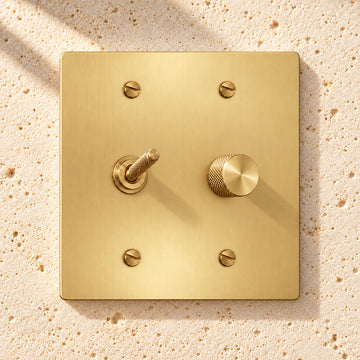2-Gang Solid Brass Knurled Toggle Light Switch & Rotary Dimmer on sunlit pale limestone
