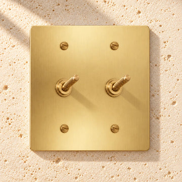 2-Gang Solid Brass Knurled Toggle Light Switches on sunlit pale limestone