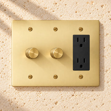 3-Gang Solid Brass 2 Rotary Dimmers + 1 Duplex Outlet on sunlit pale limestone