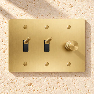3-Gang Knurled Brass Toggle Light Switches & Rotary Dimmer on sunlit pale limestone