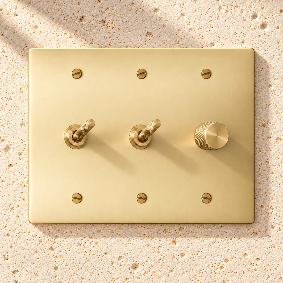 3-Gang Solid Brass 2 Knurled Toggle Light Switches & Dimmer on sunlit pale limestone