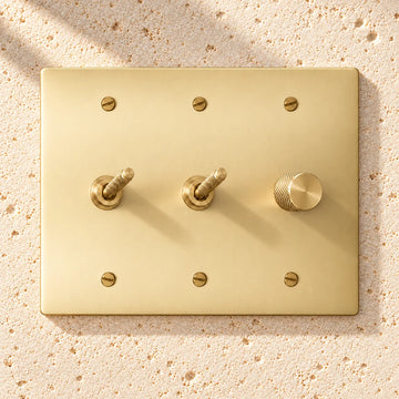 3-Gang Solid Brass 2 Knurled Toggle Light Switches & Dimmer on sunlit pale limestone