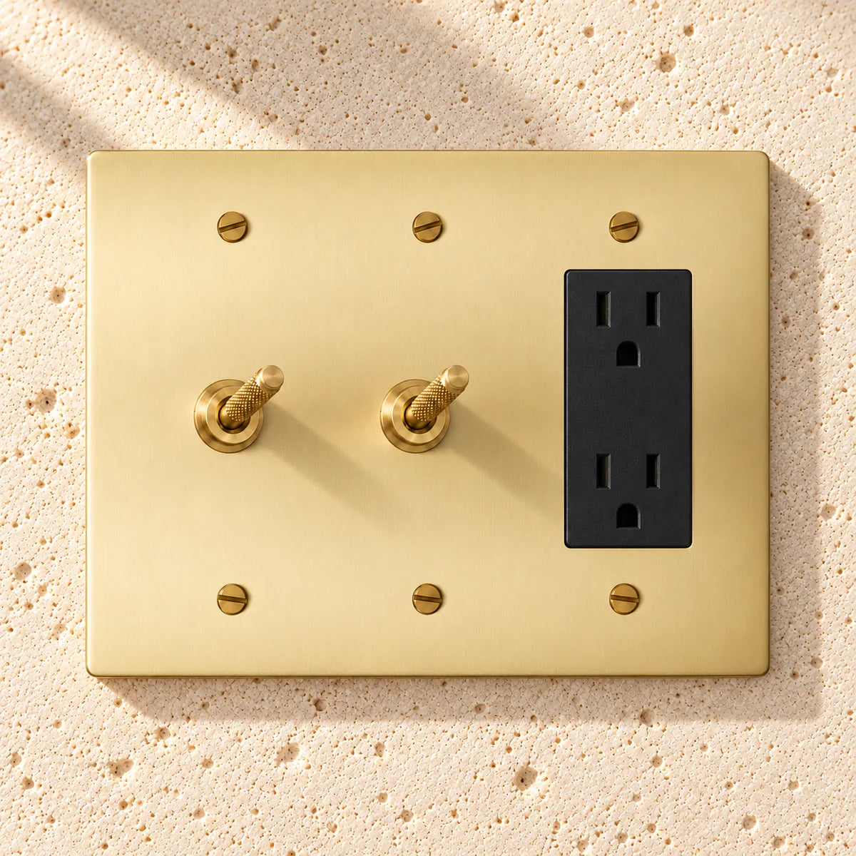3-Gang Solid Brass 2 Knurled Toggle Light Switches & Duplex Outlet on sunlit pale limestone