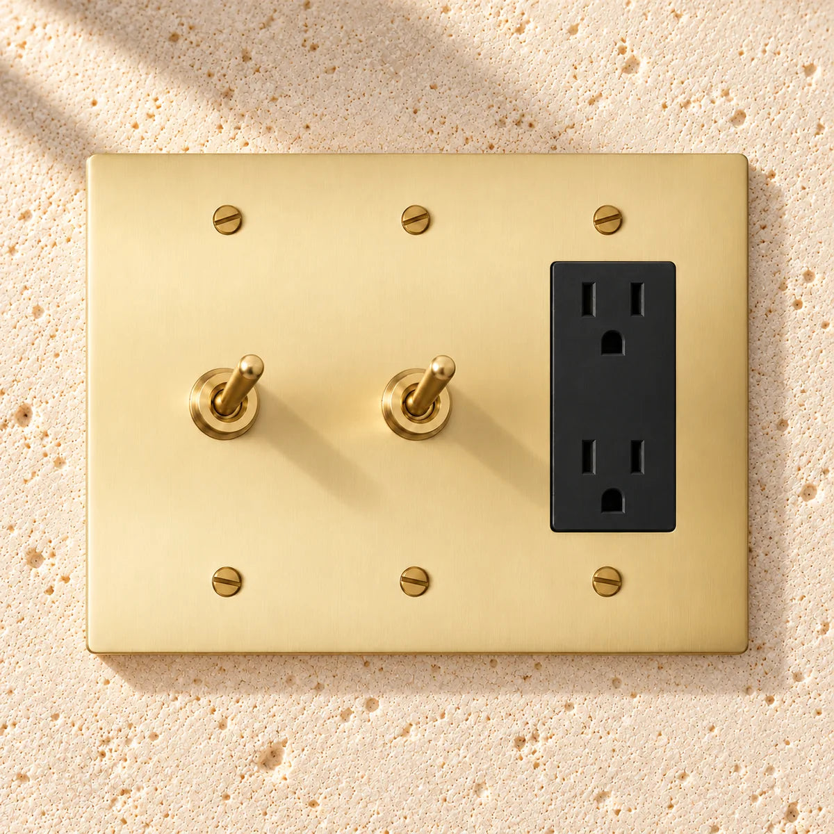 3-Gang Solid Brass 2 Toggle Light Switches & Duplex Outlet on sunlit pale limestone
