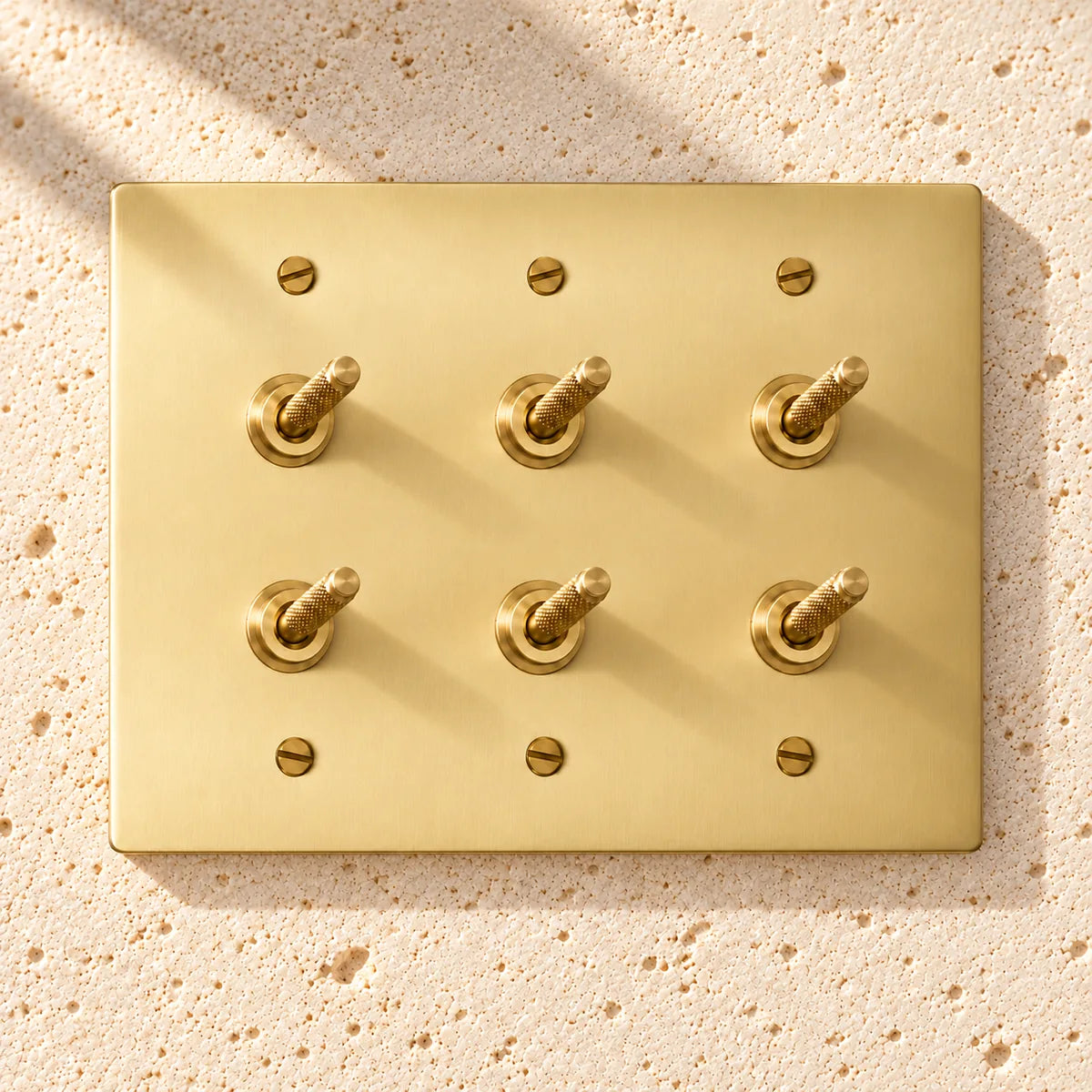 3-Gang Solid Brass Double Knurled Toggle Light Switches on sunlit pale limestone