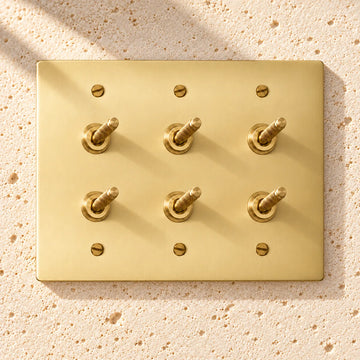 3-Gang Solid Brass Double Knurled Toggle Light Switches on sunlit pale limestone