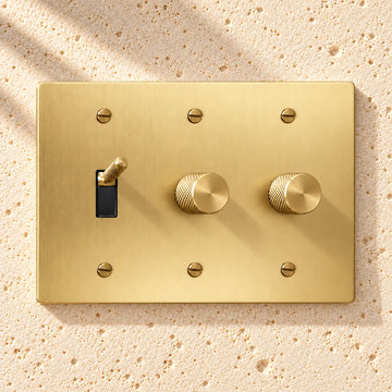 3-Gang Knurled Brass Toggle Light Switch & 2 Rotary Dimmers on sunlit pale limestone