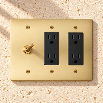 3-Gang Solid Brass Knurled Toggle Light Switch & 2 Duplex Outlets on sunlit pale limestone