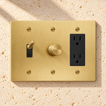 3-Gang Knurled Brass Toggle Light Switch, Dimmer & Duplex Outlet on sunlit pale limestone