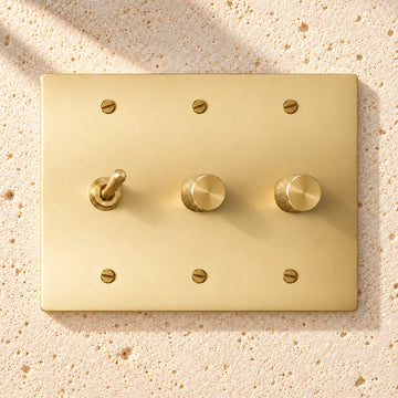 3-Gang Solid Brass Toggle Light Switch & 2 Rotary Dimmers on sunlit pale limestone