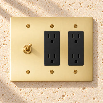 3-Gang Solid Brass Toggle Light Switch & 2 Duplex Outlets on sunlit pale limestone