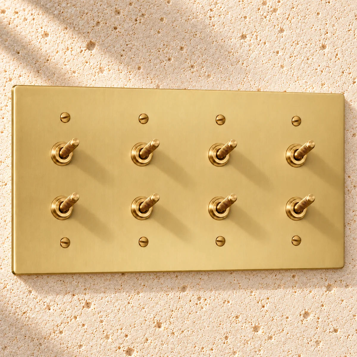 4-Gang Solid Brass Double Knurled Toggle Light Switches on sunlit pale limestone