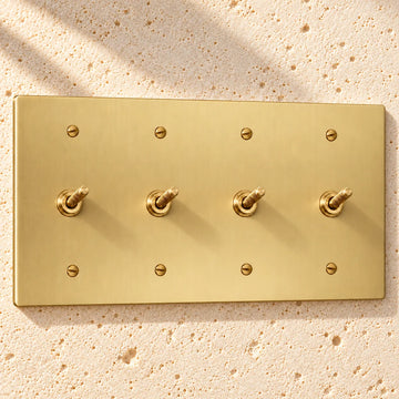 4-Gang Solid Brass Knurled Toggle Light Switches on sunlit pale limestone