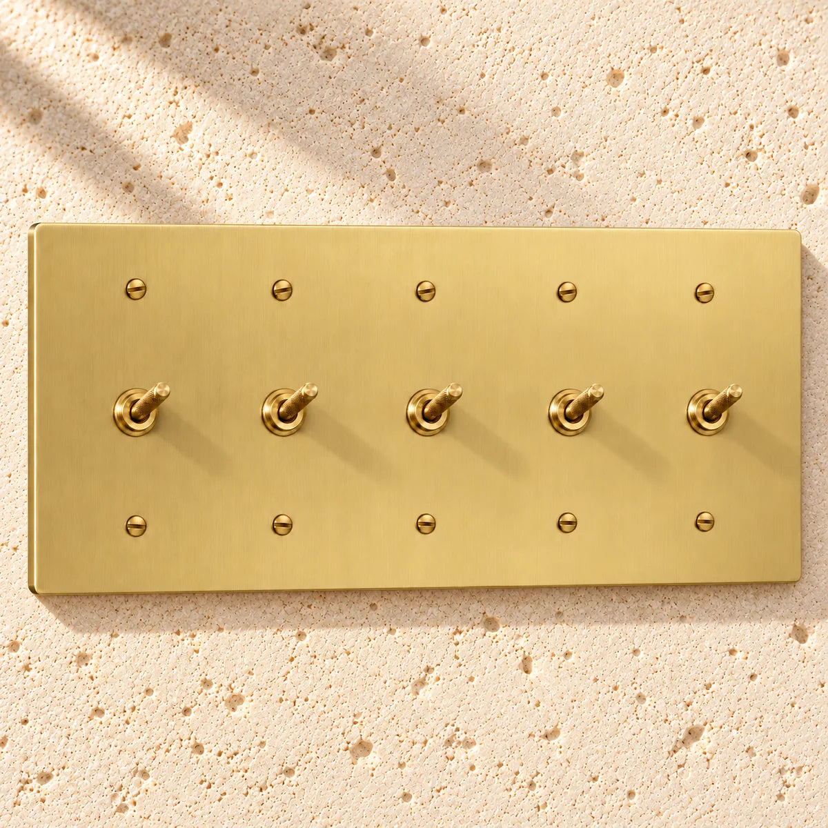 5-Gang Solid Brass Knurled Toggle Light Switches on sunlit pale limestone