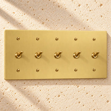 5-Gang Solid Brass Toggle Light Switches on sunlit pale limestone