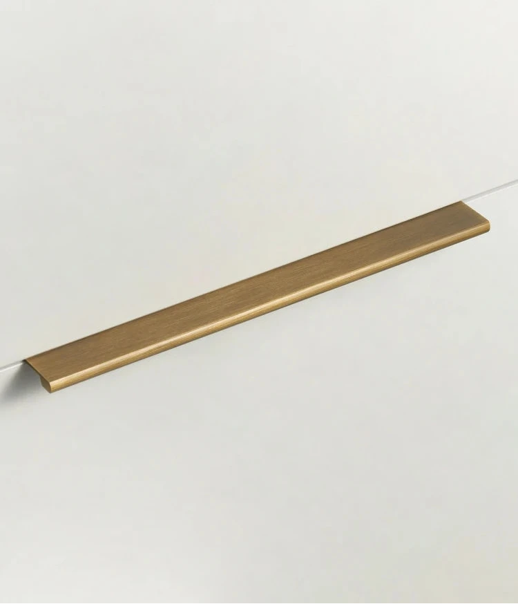 Antique brass cabinet edge pull on a drawer of beige cupboard.