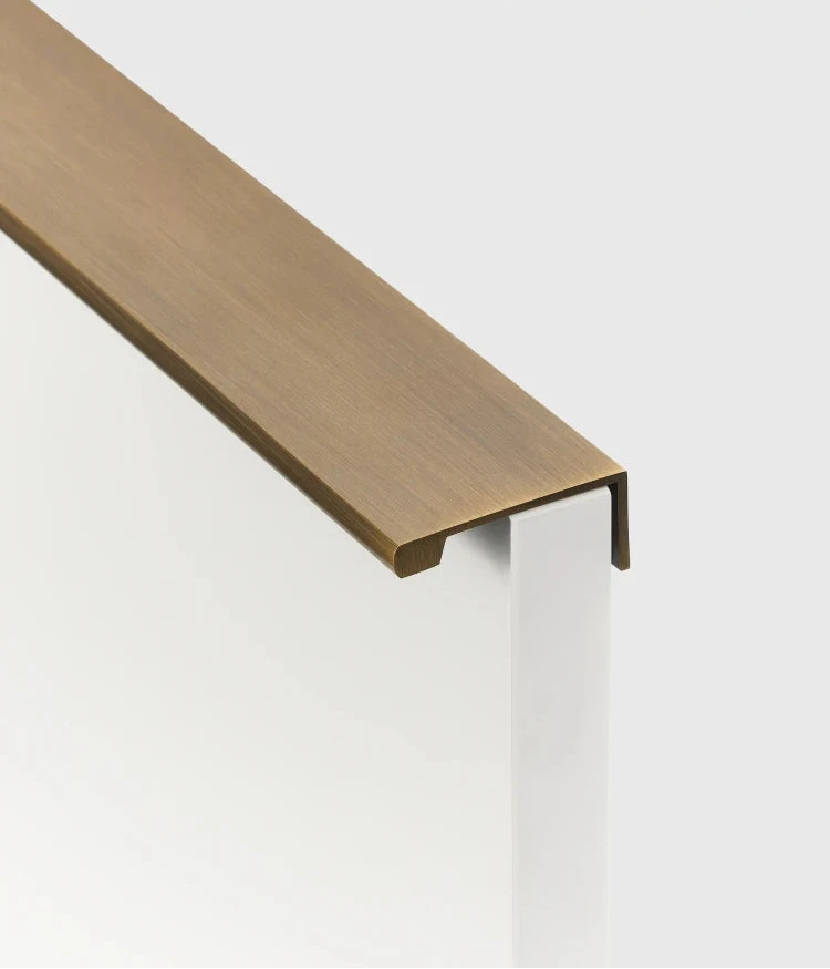 Antique brass cabinet edge pull on a drawer of beige cupboard shown from a side.