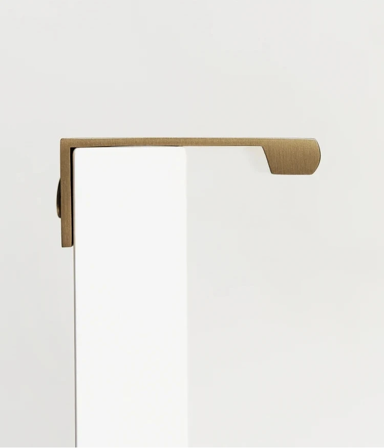 Antique brass cabinet edge pull on a drawer of beige cupboard shown from a backside.