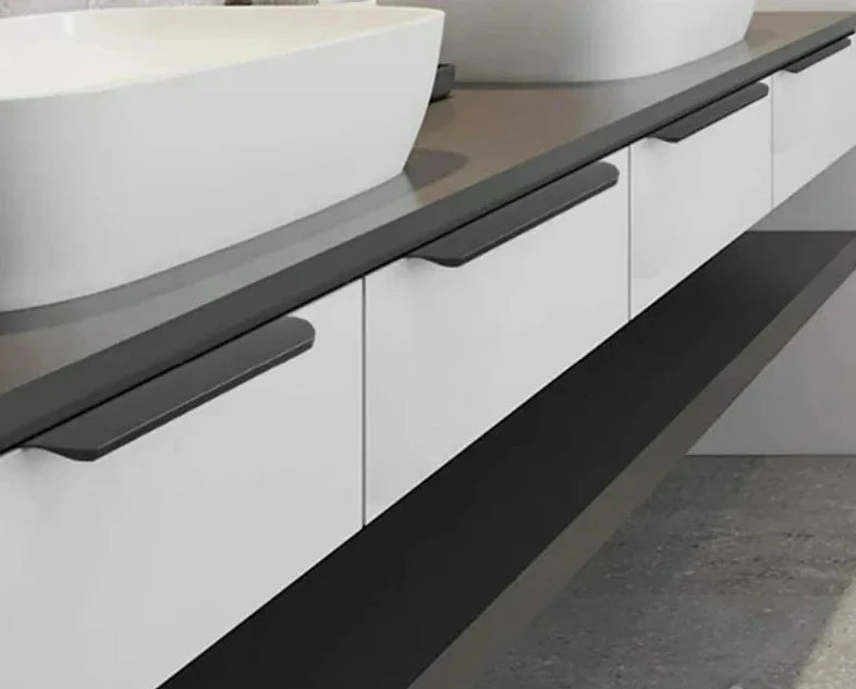 Bathroom vanity with black hidden edge pulls, white sinks and black countertop.