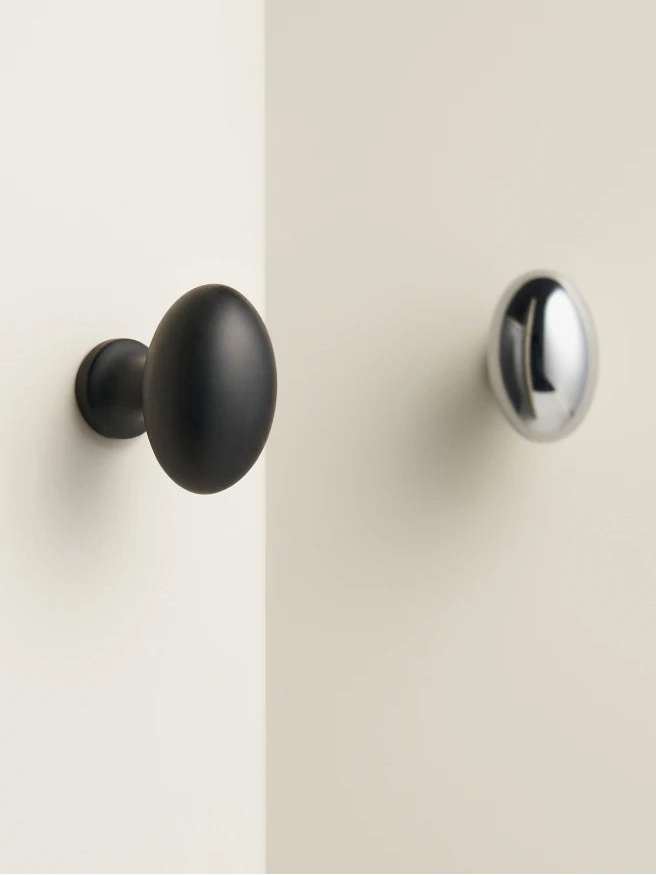 Two cabinet knobs, one black and one silver, on a white door.