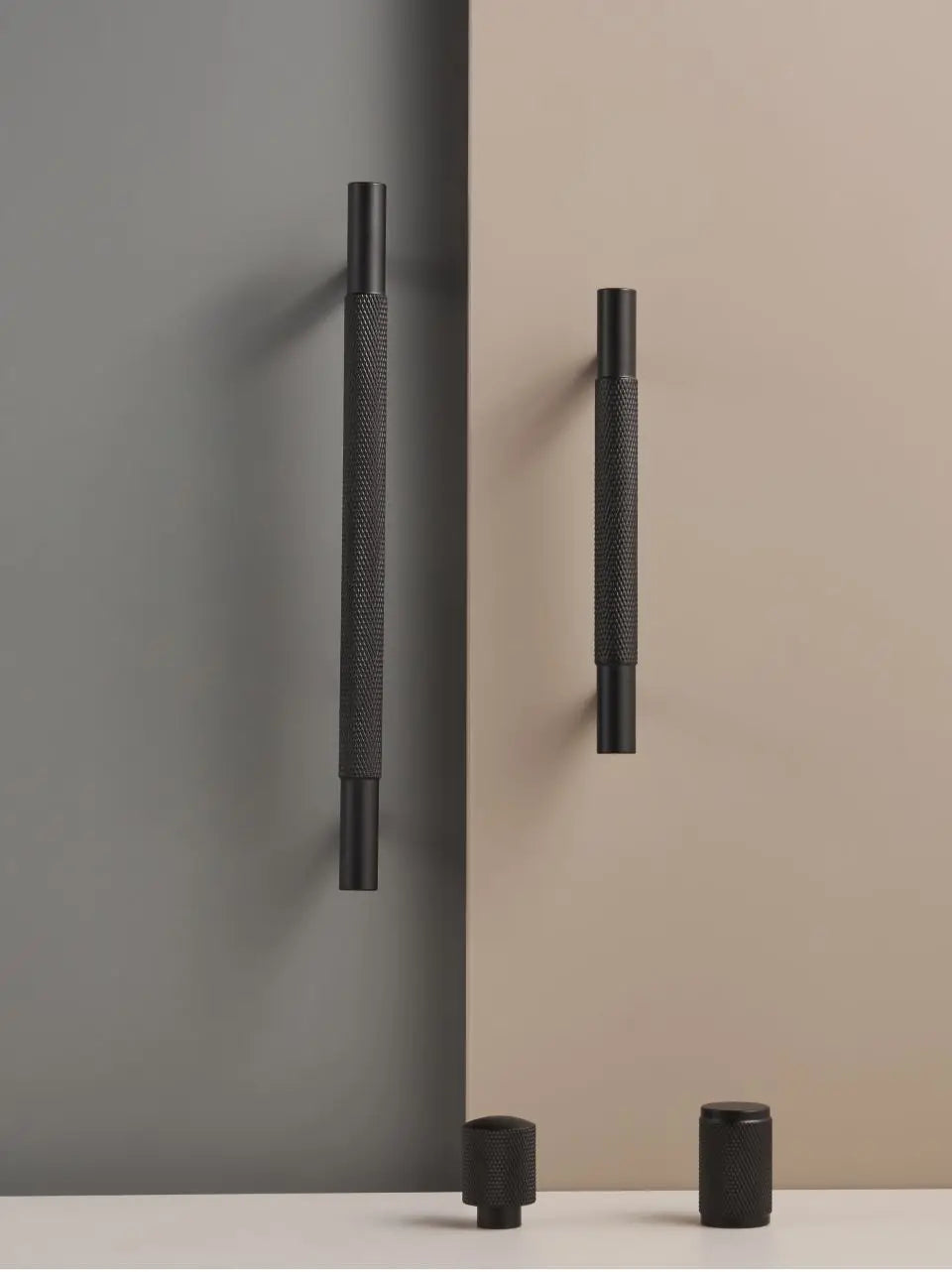 Black cross knurled door handles and knobs on a grey and beige wall.