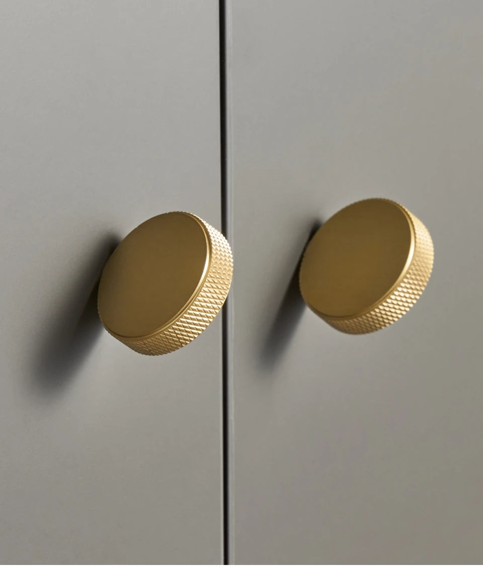 Two gold anti-slip cabinet knobs on a light grey door.