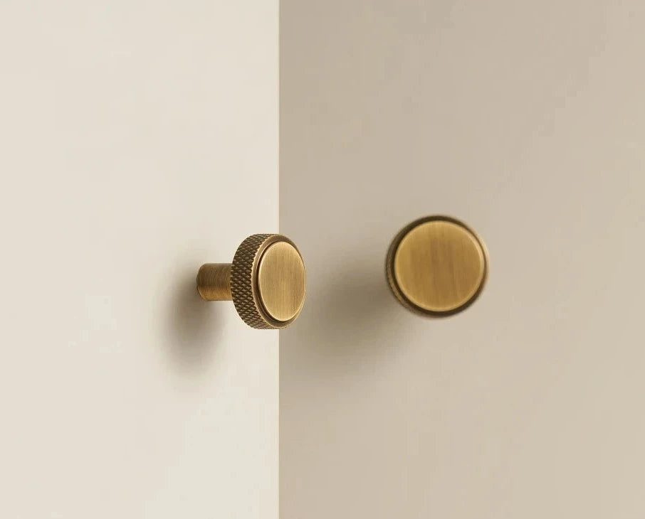 Four knurled brass knobs in black, gold, antique bronze and silver on a beige surface.