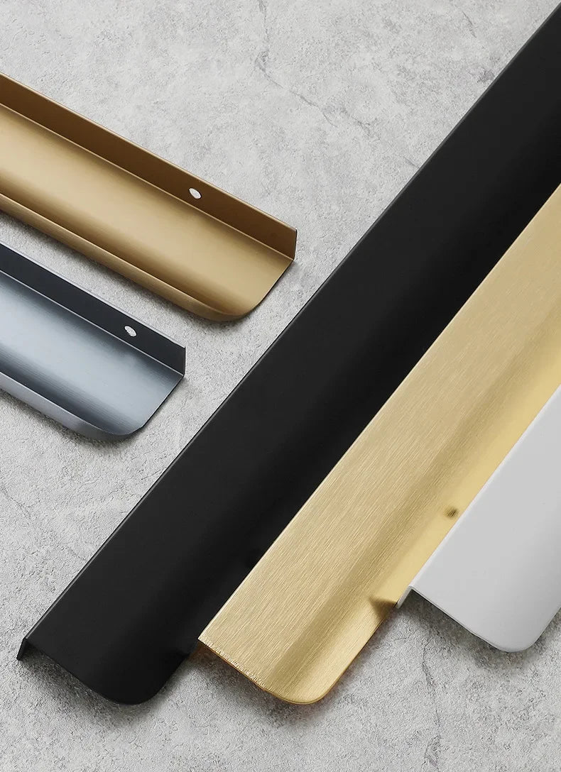 Aluminium edge pull samples in gold, black, grey, white and bronze on a grey concrete surface.