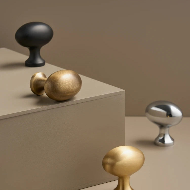 Decorative cabinet knobs in gold, black, and silver on a beige surface.