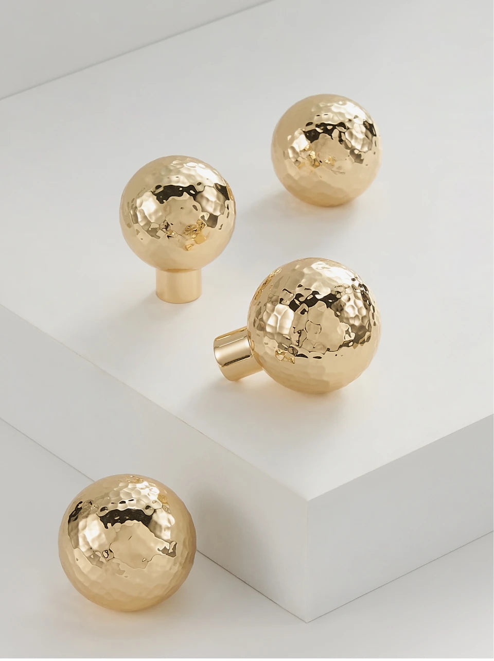 Four gold brass hammered knobs on a white surface.