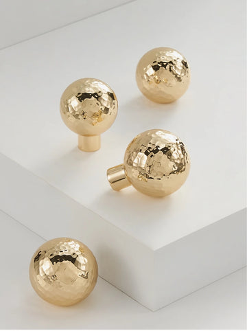 Four gold brass hammered knobs on a white surface.